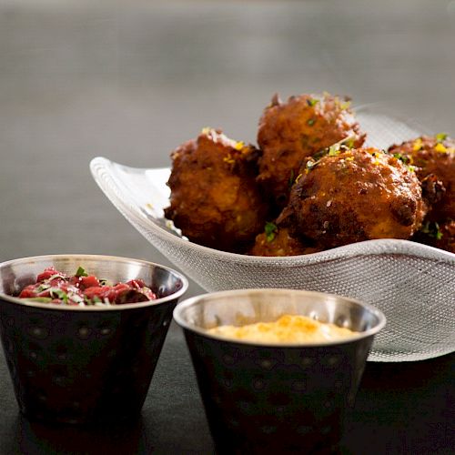 The image shows a dish of fried balls accompanied by two small bowls of dipping sauces, one dark and one yellow in color.