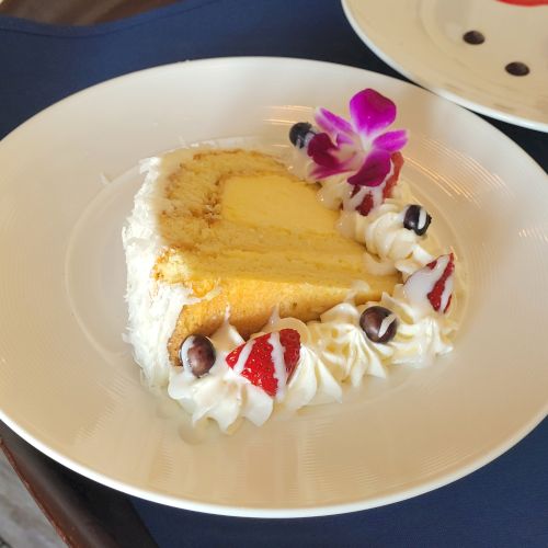 A slice of cake garnished with whipped cream, strawberries, blueberries, and a purple orchid on a white plate.