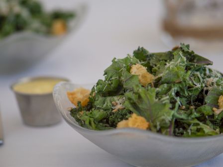 The image shows a fresh green salad served in a bowl, accompanied by a small container of dressing on the side.