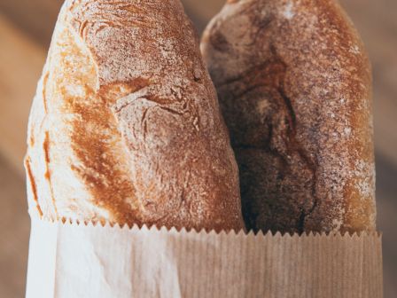 The image shows two loaves of bread in a brown paper bag.