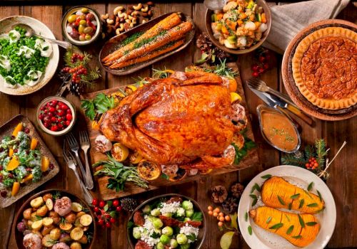 This image shows a Thanksgiving spread with roast turkey, various vegetables, salads, bread, pie, and assorted side dishes on a wooden table.