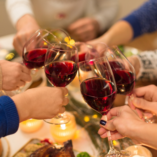A group of people clinking glasses of red wine together in a celebratory toast over a table with candles and food, creating a festive atmosphere.