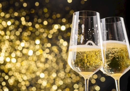 Two champagne glasses filled with bubbly champagne, with a bokeh background of golden lights, creating a festive atmosphere.
