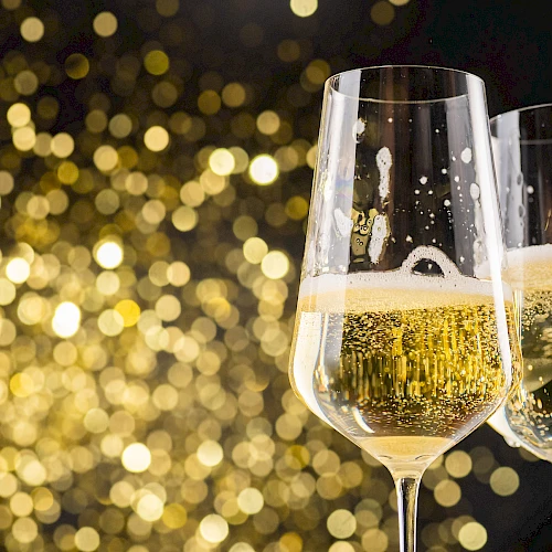 Two champagne glasses filled with bubbly champagne, with a bokeh background of golden lights, creating a festive atmosphere.