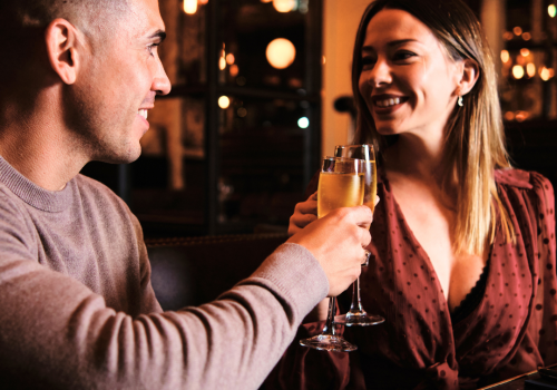 A couple is smiling and toasting with champagne glasses in a warmly lit restaurant.