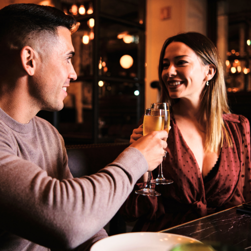 A couple is smiling and toasting with champagne glasses in a warmly lit restaurant.